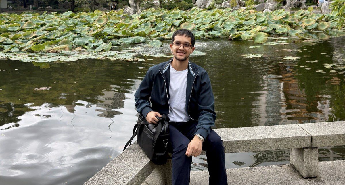 Abiral Khadka sitting by the lotus pond at the Chinese Garden of Friendship, with the Sydney skyline behind